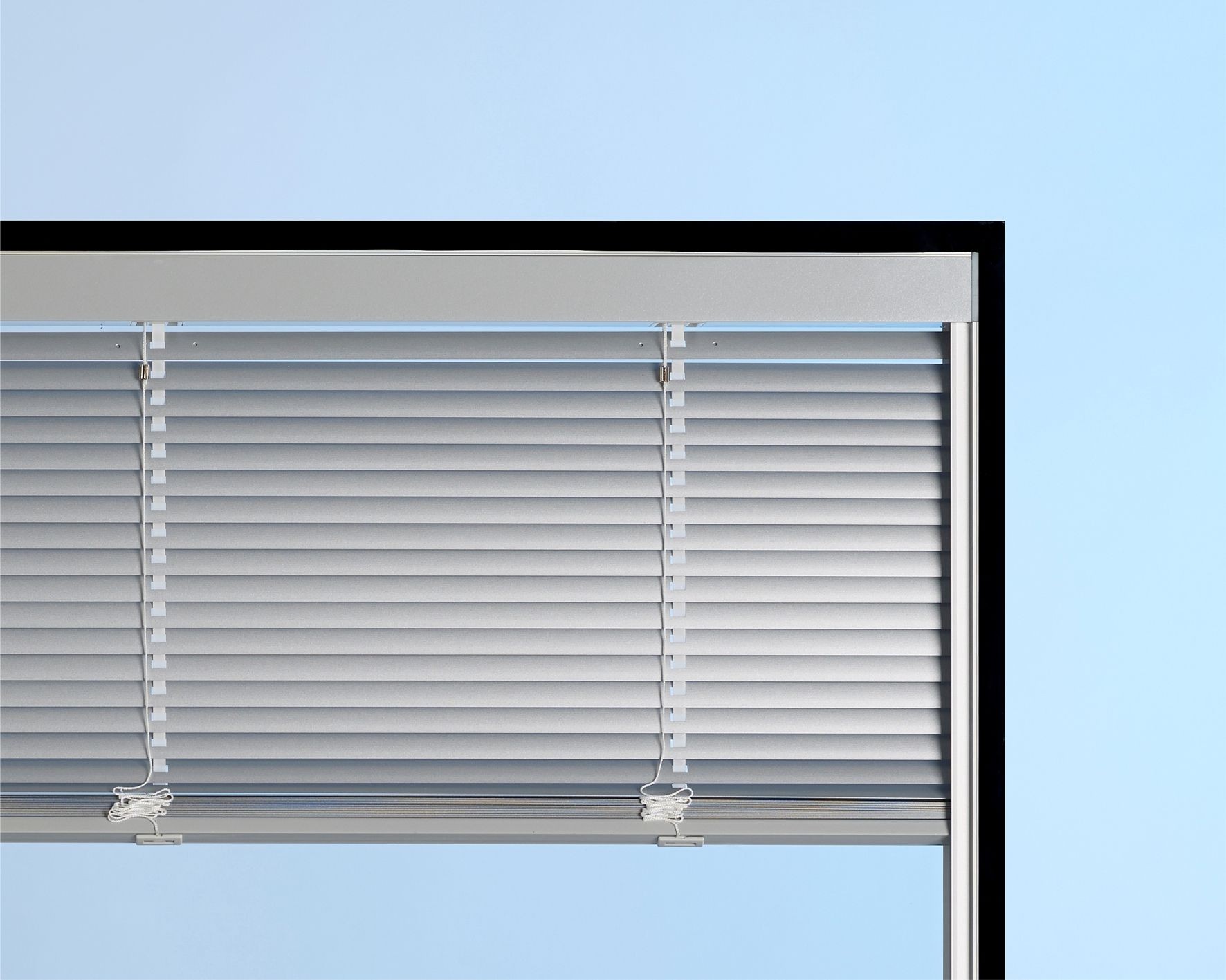 Close-up of an aluminum venetian blind partially closed against a light blue background.