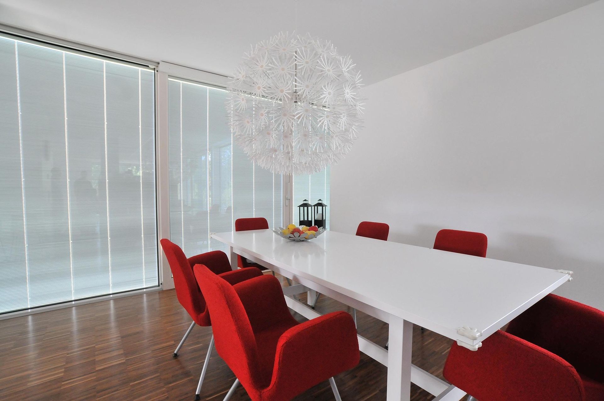 Modern dining room with white table, red chairs, and an intricate chandelier.